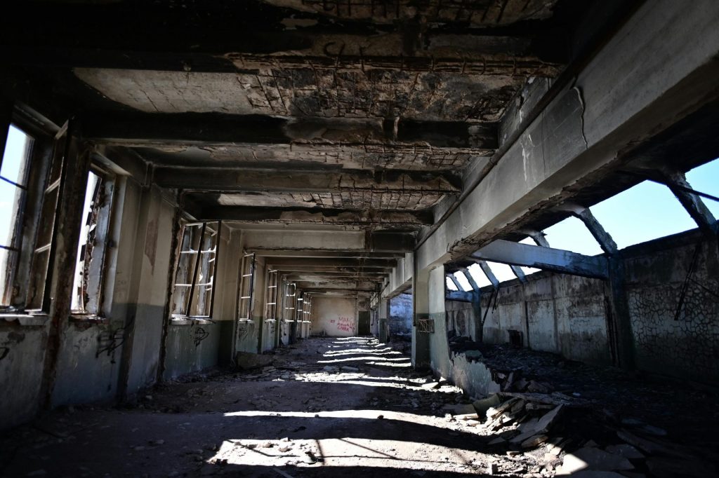 An abandoned industrial building with broken windows and structural decay under clear daylight.